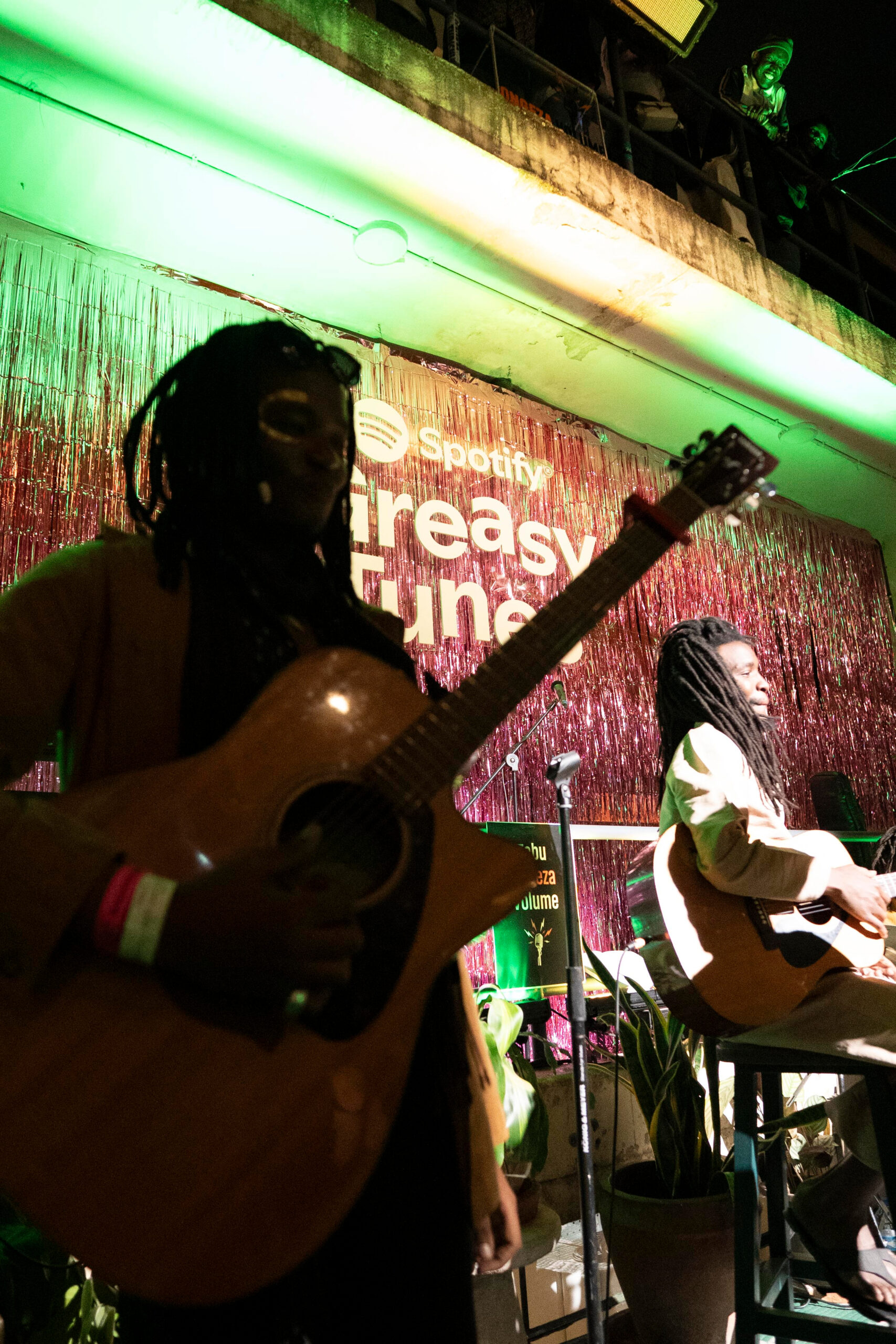 Guitarists performing on stage under green lighting at Spotify's Greasy Tunes Nairobi