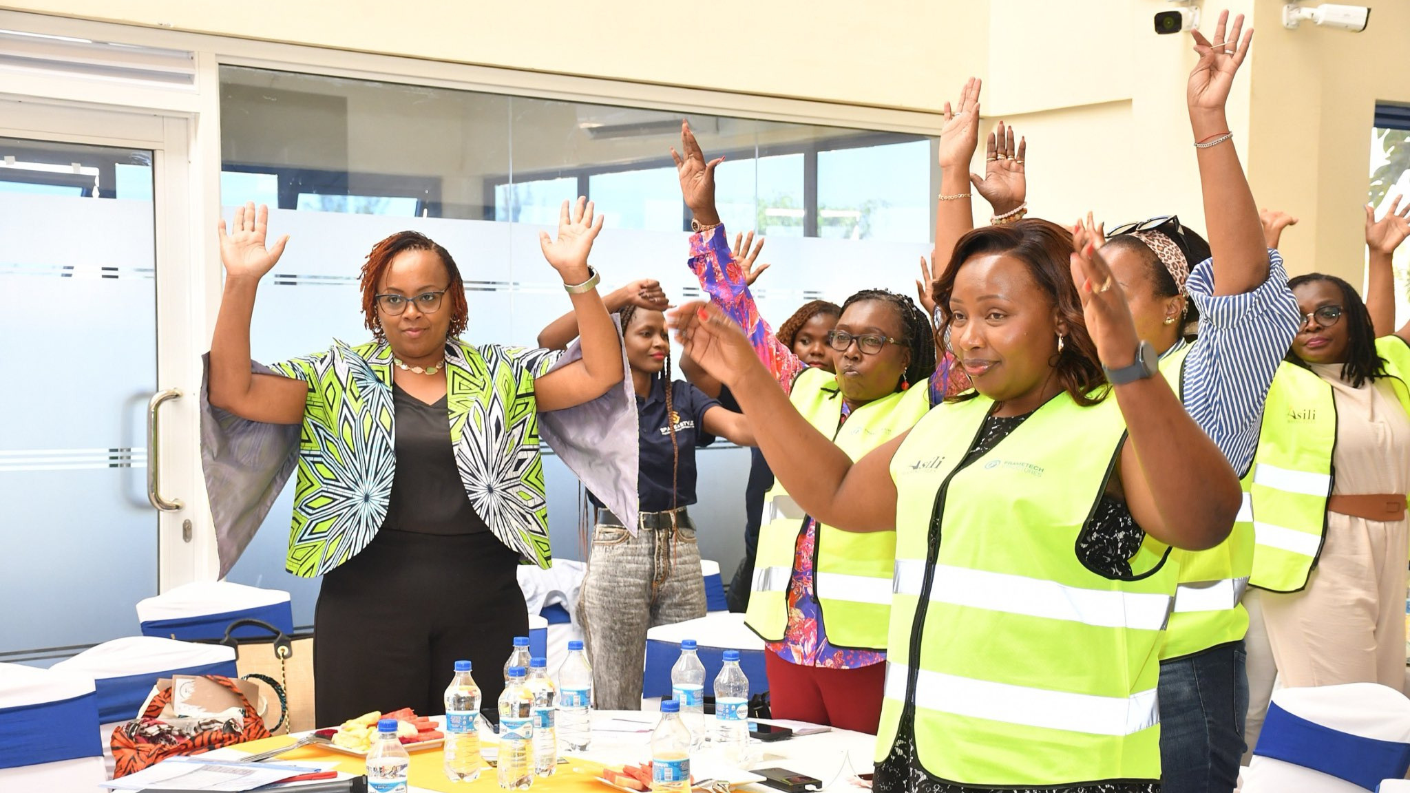 Participants and attendees—wearing branded safety vests—engaging in an interactive session with raised hands inside the venue.