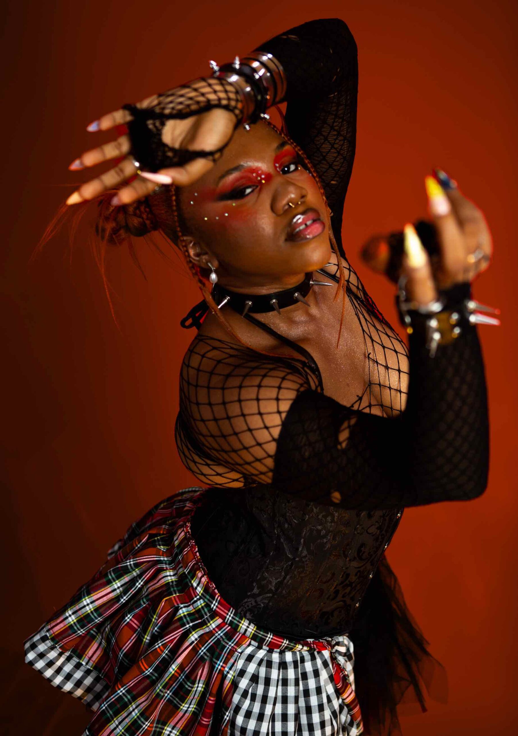 AfroReekAH in fishnet sleeves, a plaid skirt and red eye makeup for a REEPLAY promotional photo