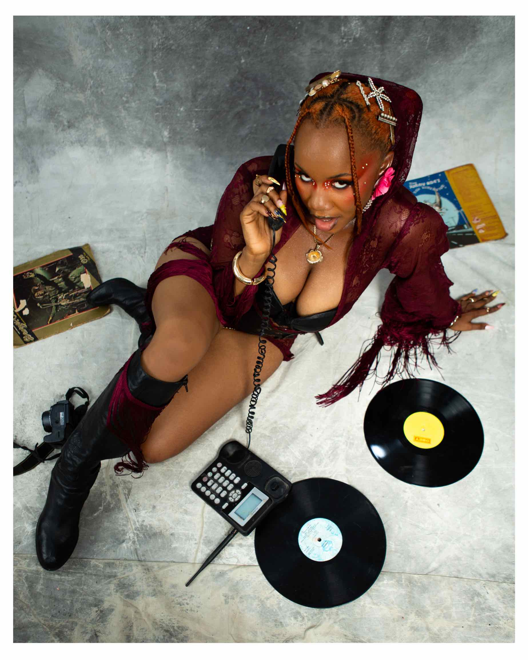 AfroReekAH on the floor with a corded phone and vinyl records in a REEPLAY promotional photo