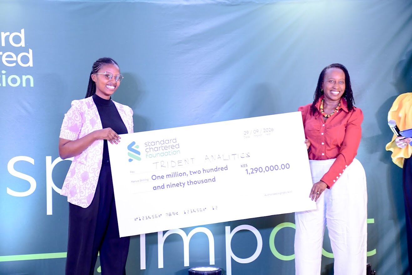 Trident Analytics founder holds a KES 1,290,000 Standard Chartered Foundation cheque on stage with a presenter