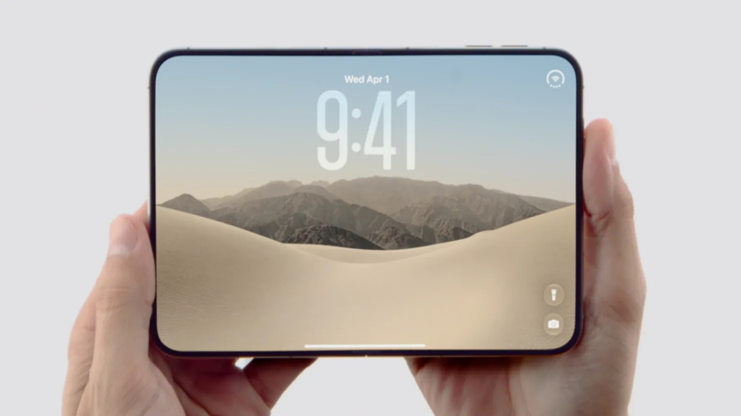 iPhone Duo unfolded in a person's hands showing the lock screen with time and desert wallpaper