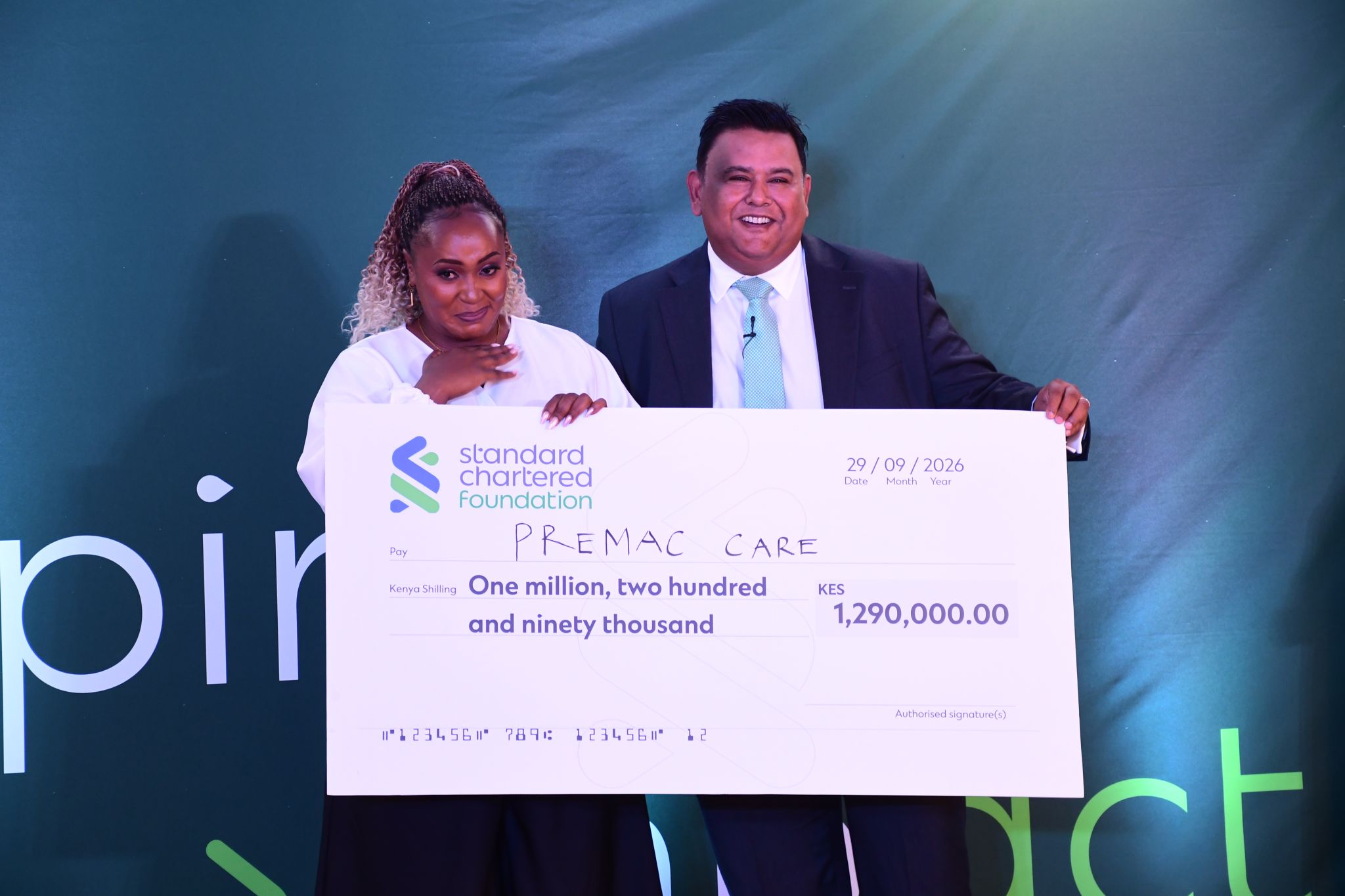 Premac Care founder and Birju Sanghrajka hold a KES 1,290,000 Standard Chartered Foundation cheque on stage