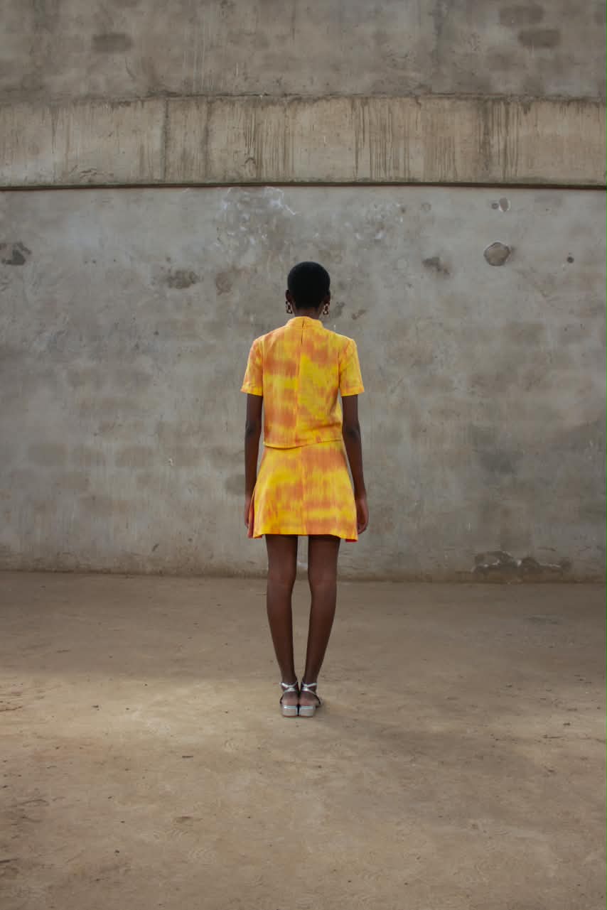 Model seen from behind in a yellow and orange dyed short sleeve top and skirt