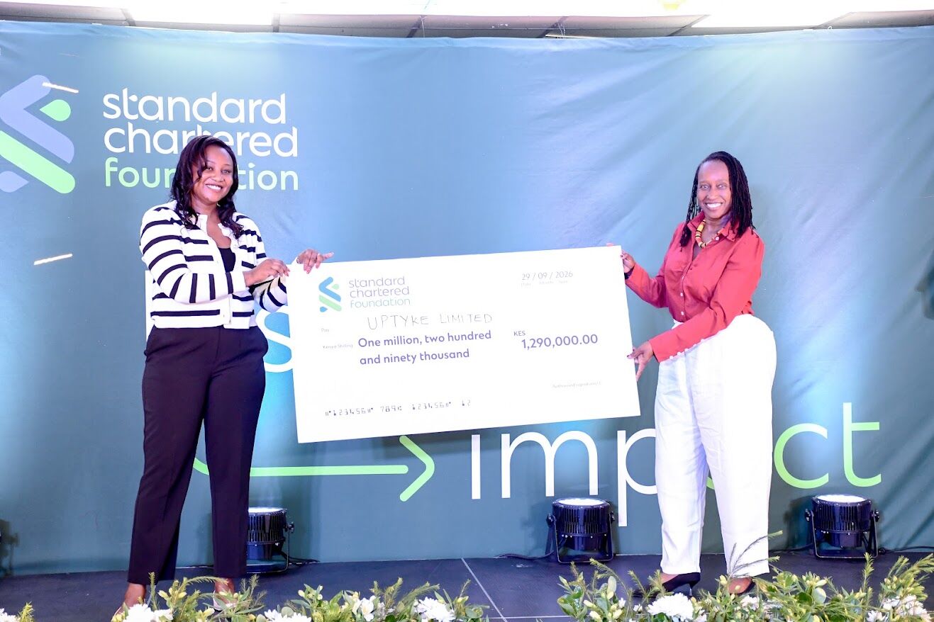 Uptyke founder holds a KES 1,290,000 Standard Chartered Foundation cheque on stage with a presenter