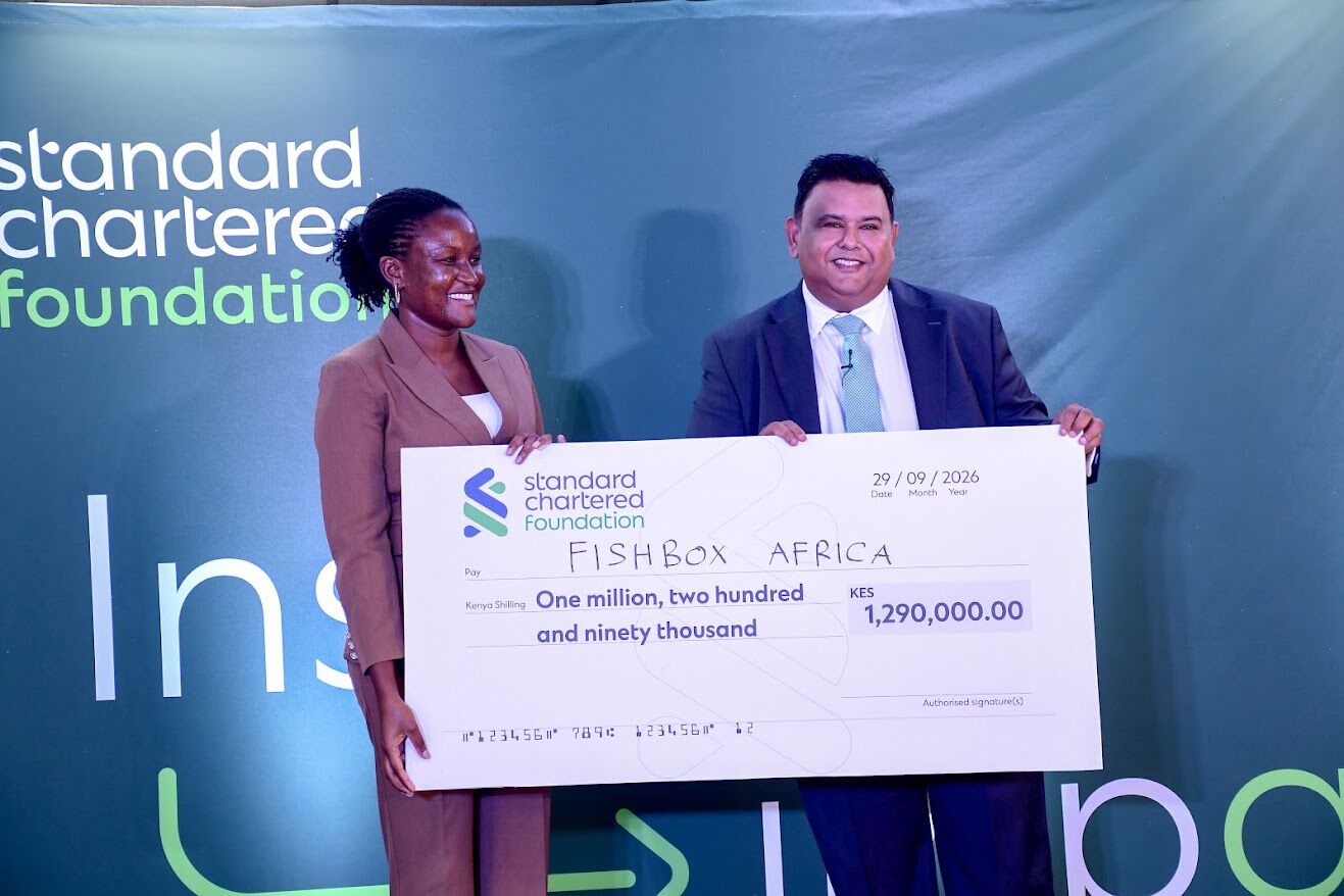 FishBox Africa co-founder holds a KES 1,290,000 Standard Chartered Foundation cheque on stage with a presenter