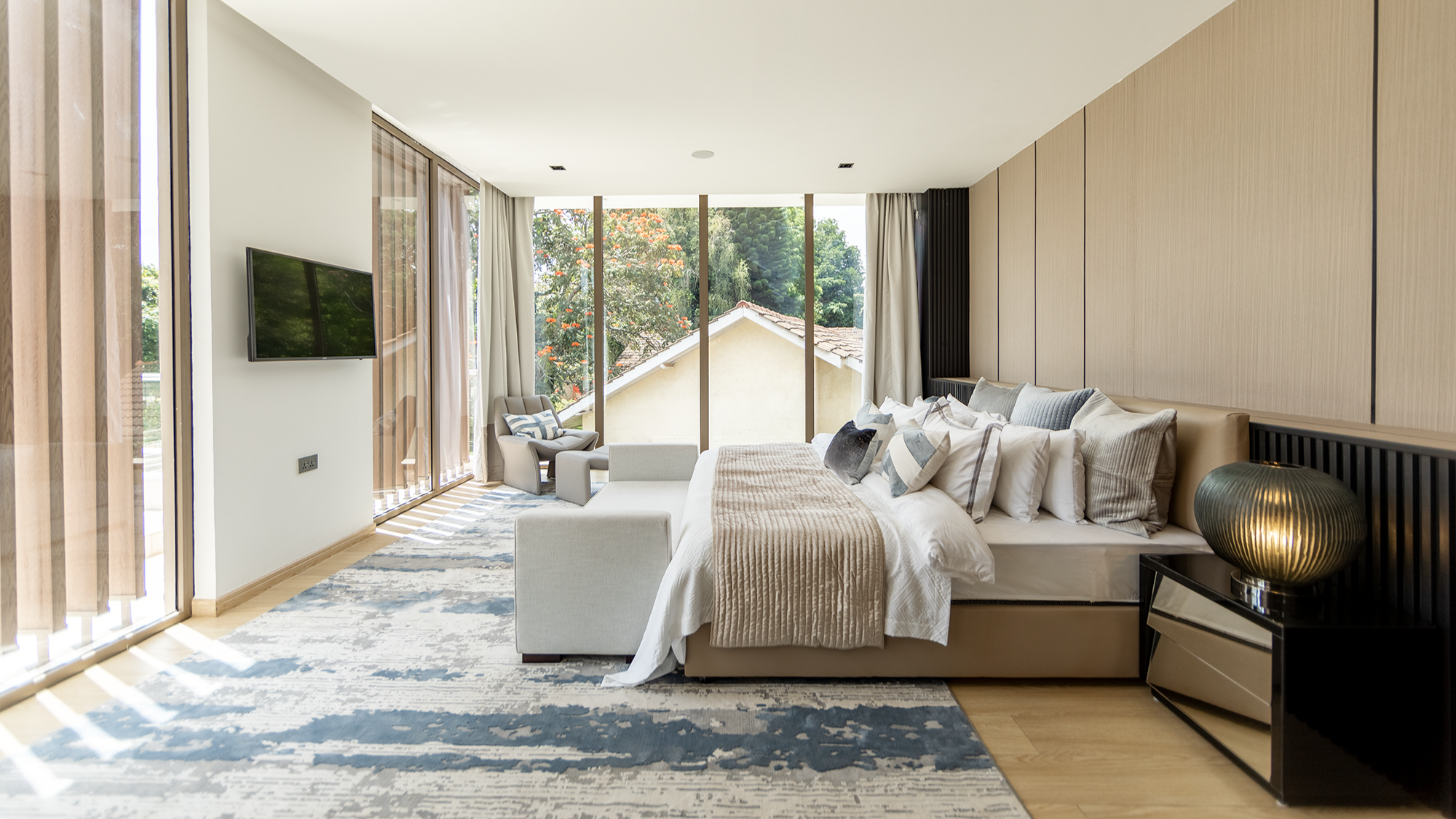 Master bedroom at Moments Villas with floor to ceiling windows, a wood panelled headboard wall and garden views.