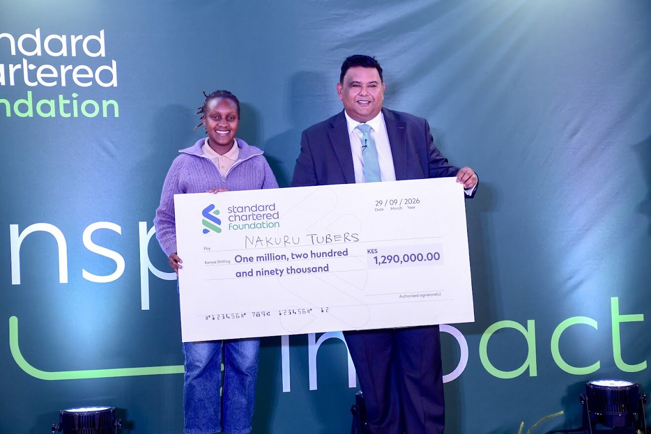 Nakuru Tubers co-founder holds a KES 1,290,000 Standard Chartered Foundation cheque on stage with a presenter