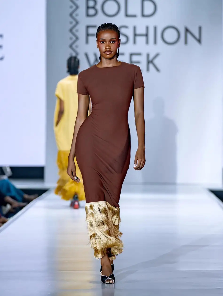 Almorie Nagayi walks the Bold Fashion Week runway in a brown fitted dress with a gold fringe hem.