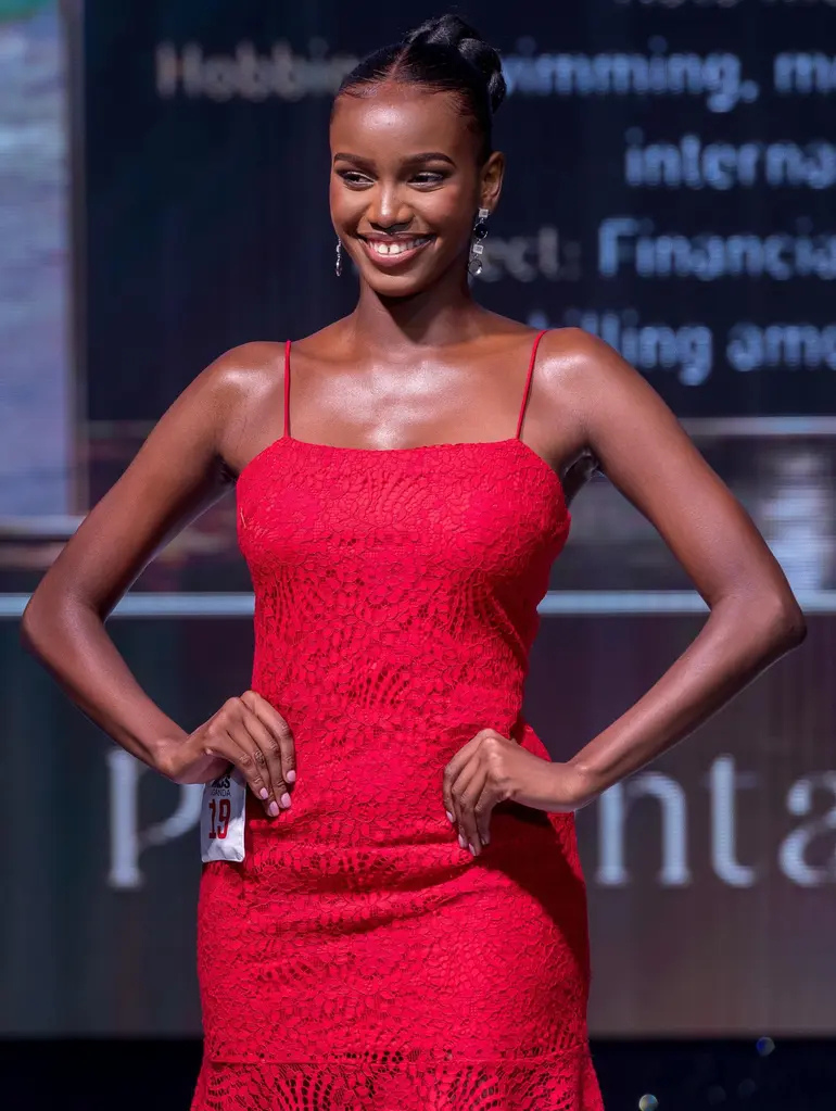 Almorie Nagayi, contestant number 19, smiles on stage in a red lace dress during the Miss Uganda 2026/27 competition.