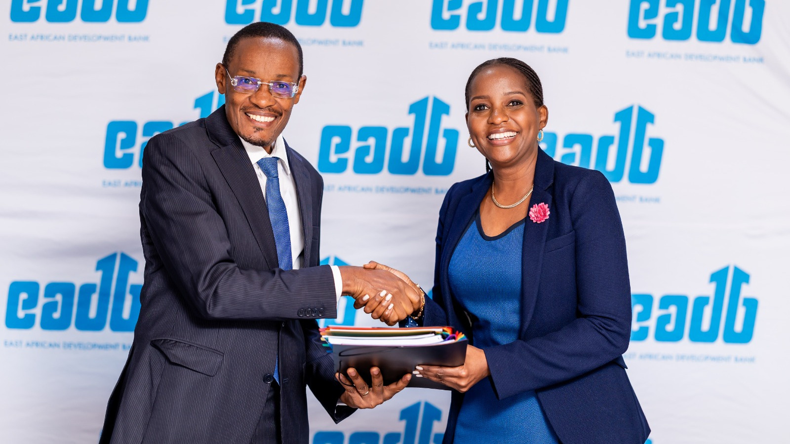 Benard Mono and Anne Juuko shake hands in front of an East African Development Bank backdrop, with Juuko holding a folder.