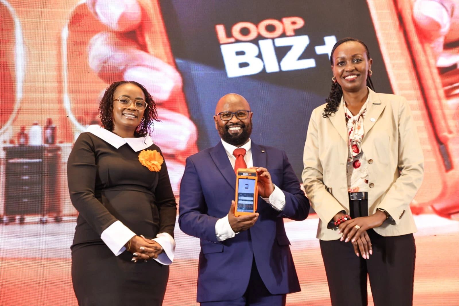Sheila Kimani, John Njoroge and Sally Chege stand on stage at the LOOP BIZ+ launch, with Njoroge holding a LOOP POS device in front of a LOOP BIZ+ backdrop.