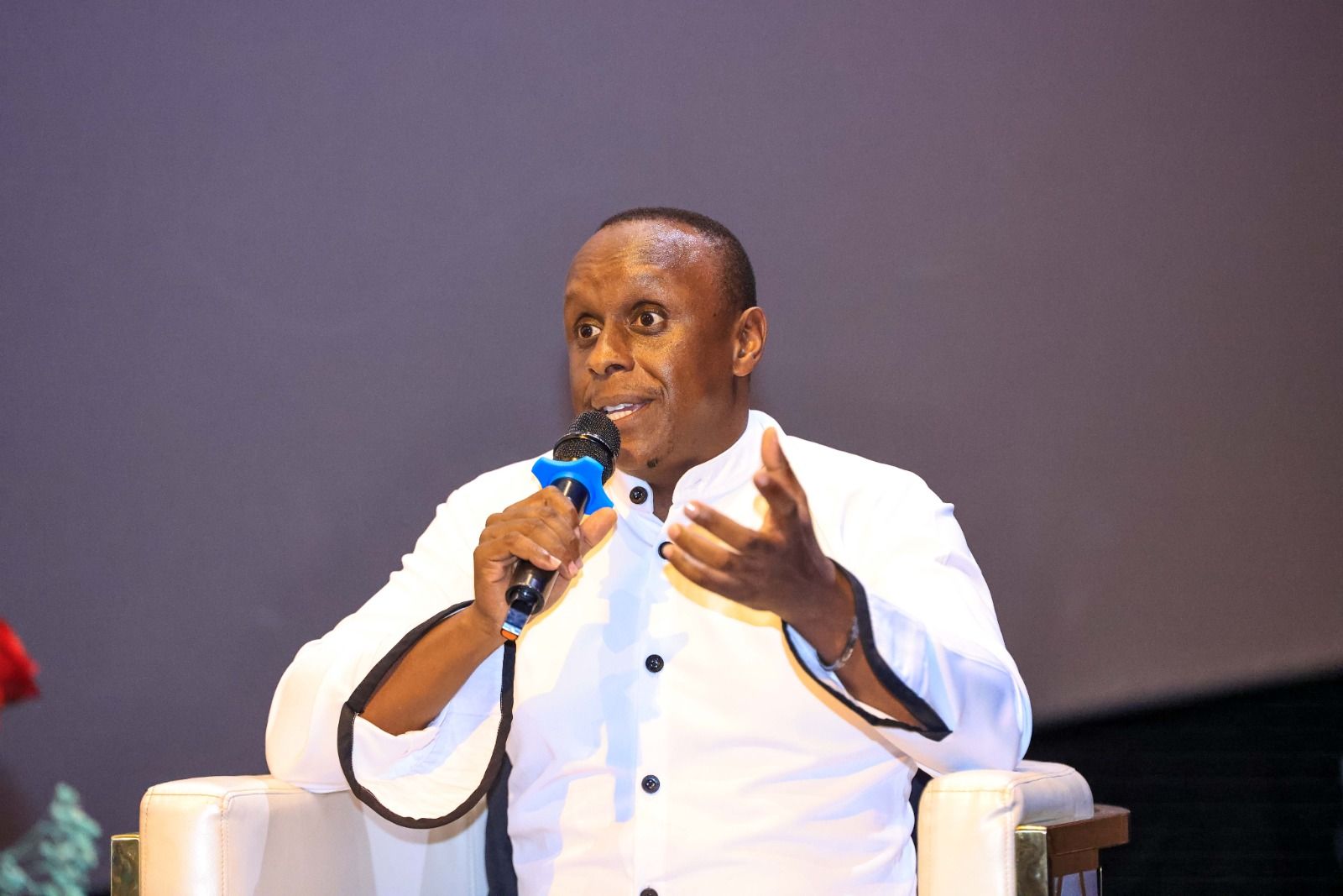 Philip Karanja, director and producer of Chamaa, speaks into a microphone while seated in a white armchair in a white shirt.