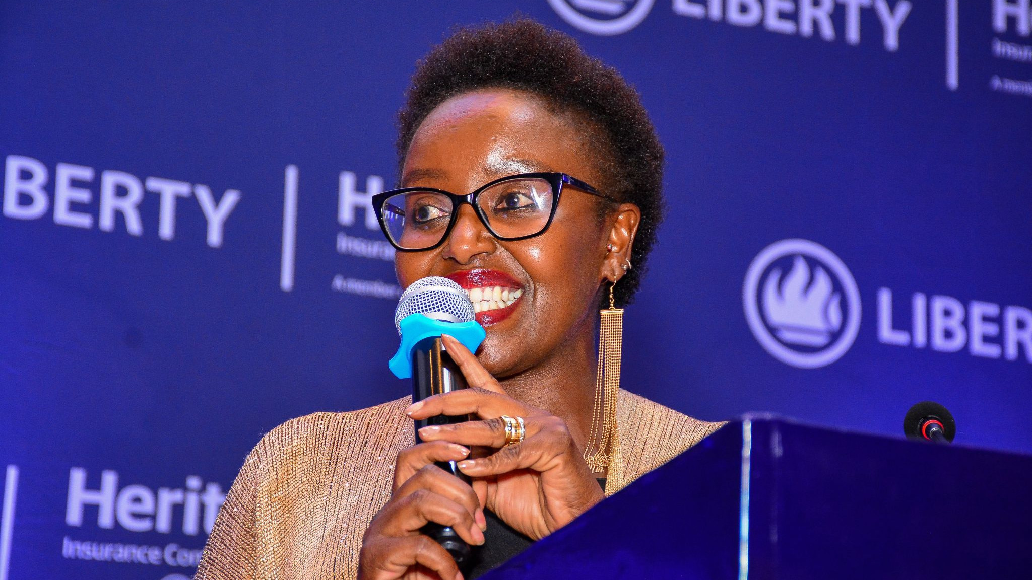 Rosalyn Mugoh speaks into a microphone at a podium in front of a Liberty and Heritage Insurance branded backdrop.