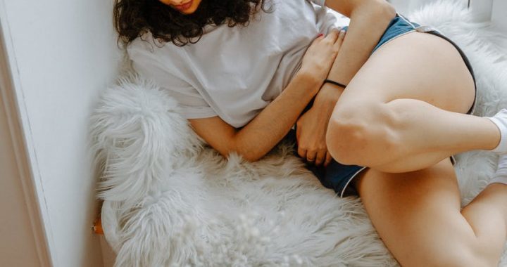 A woman on the bed touching her belly due to menstrual cramps.