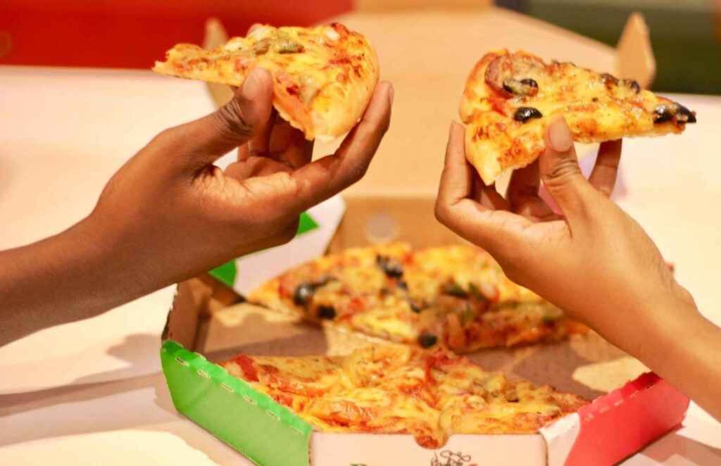 People holding pizza. Chicken is the most favoured pizza topping in Kenya