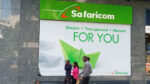 Kenyans walking near a Safaricom poster celebrating customer growth in Kenya and Ethiopia with branded banners and digital devices