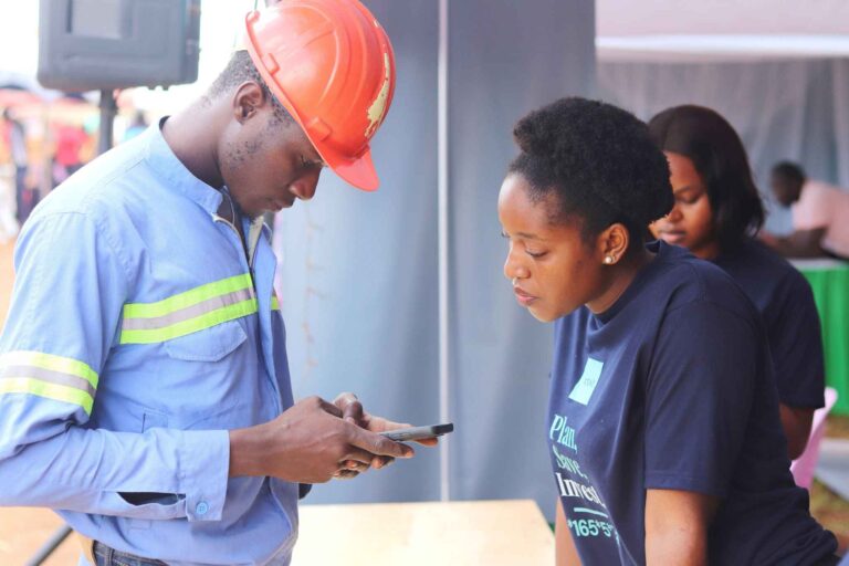 Unlocking Africa’s Investment Potential: How Boost Africa Helped XENO Investments Scale and Transform Financial Inclusion - XENO representative reviewing mobile app with field worker - Title: On-Site Engagement with XENO Investment App - Caption: A XENO team member demonstrates the investment app to a field worker during an outreach event, showcasing mobile-first financial planning. - Description: The image shows a construction worker in safety gear interacting with a XENO representative. They are reviewing something on a smartphone, likely the XENO app. This moment illustrates XENO’s commitment to reaching underserved populations with accessible, tech-enabled financial solutions.