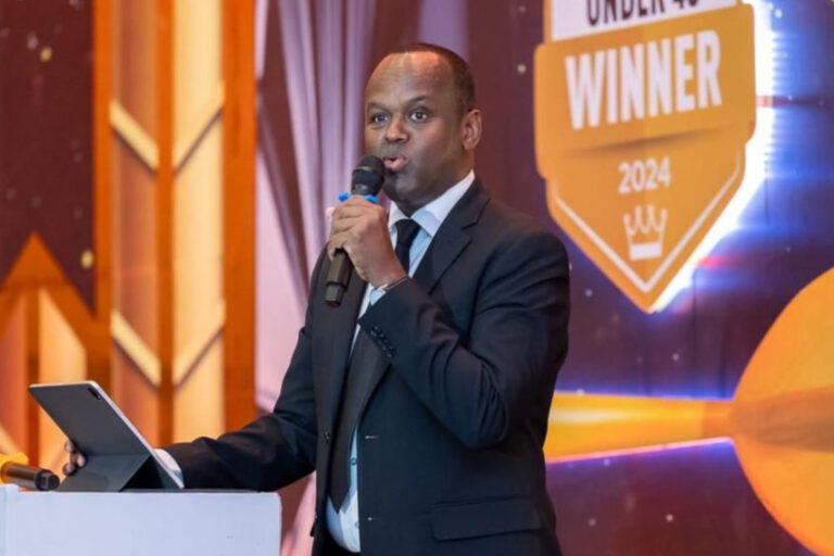 Abdi Mohamed speaking at a podium with a microphone at an awards ceremony, with an Under 40 Winner 2024 backdrop behind him