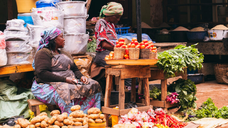 Woman vendor sitting among tomatoes, potatoes and vegetables at an East African open air market