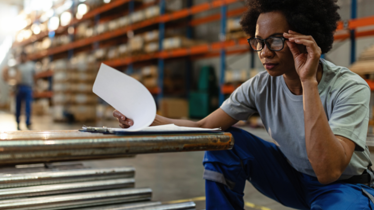Get Business Equipment Financed in 48 Hours Woman in a warehouse checking metal equipment stock against paperwork on a clipboard