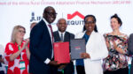 IFAD and Equity Group representatives shake hands while holding signed folders at the ARCAFIM partnership signing ceremony, with delegates applauding in the background.