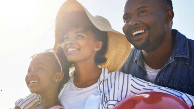 Old Mutual Revamps Savings Products to Deepen Long Term Financial Wellness A father, mother and daughter smile at the beach, holding a beach ball, backlit by sunlight