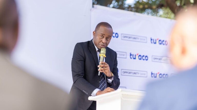 Turaco Names Cedrick Todwell Chief Commercial Officer Africa Cedrick Todwell speaks into a microphone at a podium in front of a Turaco and Opportunity Bank backdrop.