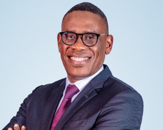 Eric Muriuki Leaves NCBA LOOP for Absa Group Eric Muriuki, who has left NCBA Group to join Absa Group, stands with arms crossed in a dark suit, purple tie and glasses against a light blue background.