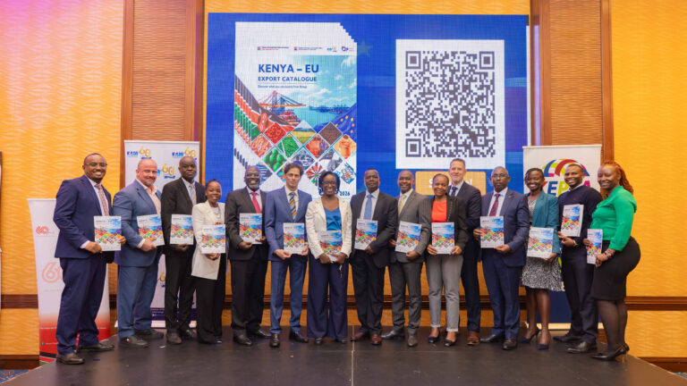 Fifteen officials and business body representatives hold the Kenya EU Export Catalogue 2026 on stage beside its cover and a QR code.