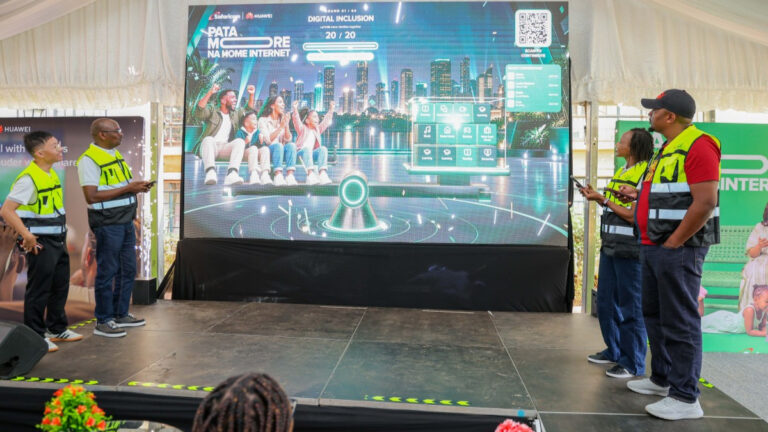 Safaricom and Huawei executives stand beside a stage screen showing the Pata More na Home Internet display